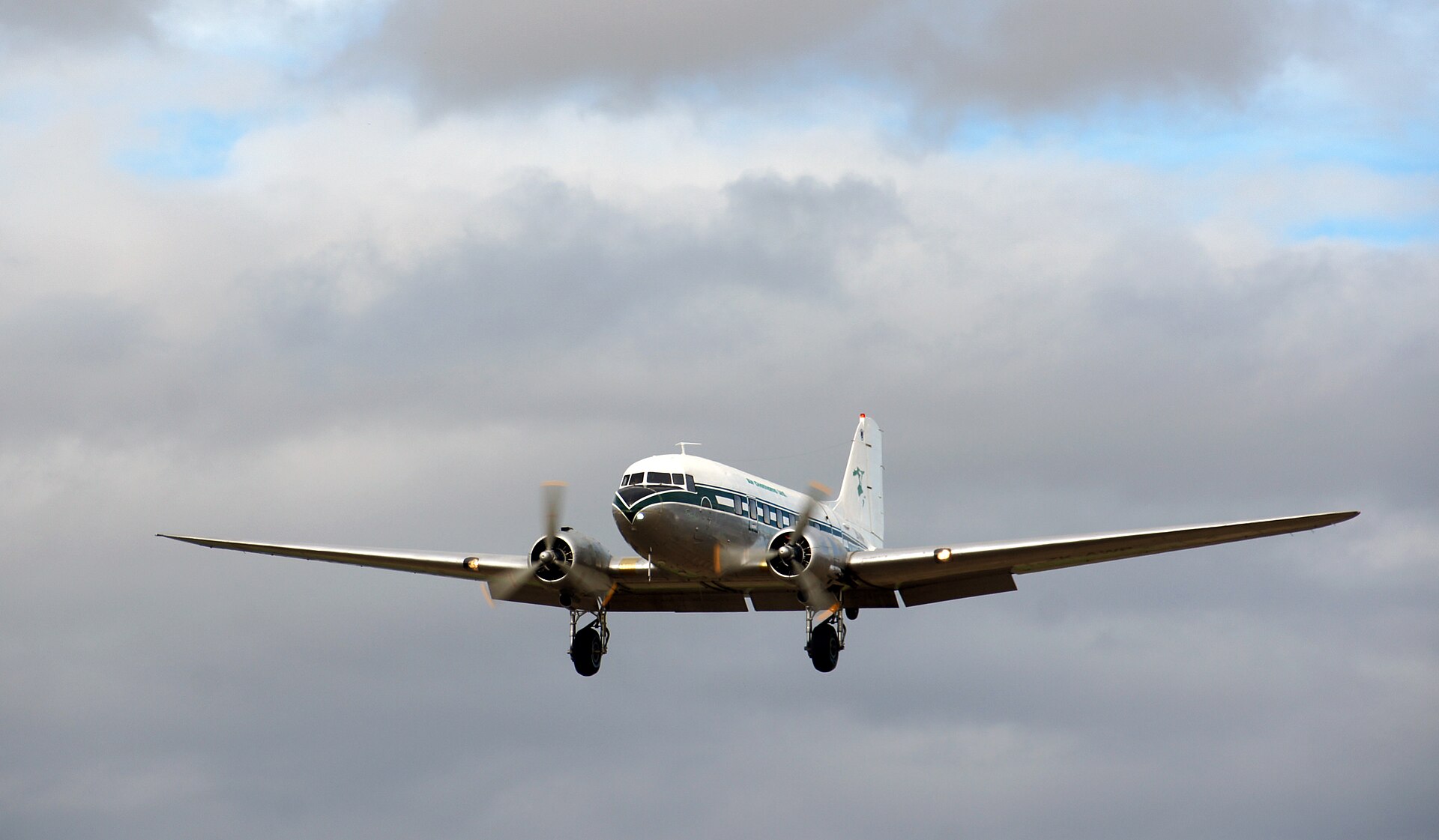 A restored Douglas DC-3 banking on approach against a cloudy sky
